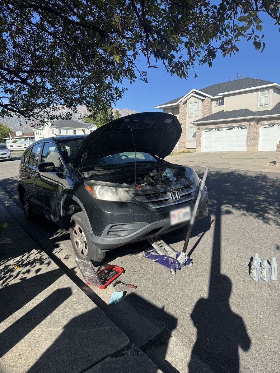 Honda CR-V with the hood up and oil bottles beside it in a driveway