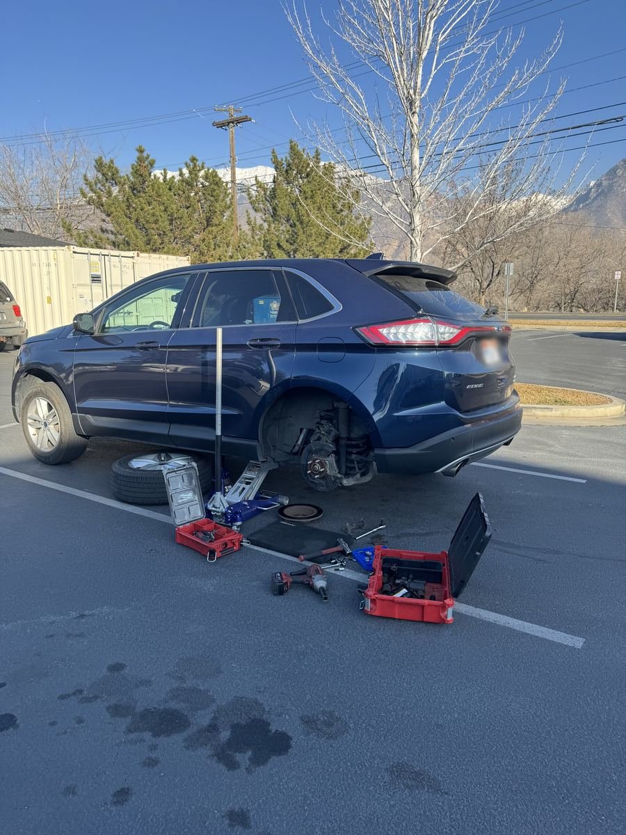 Ford Edge on a jack with a rear wheel off in a parking lot