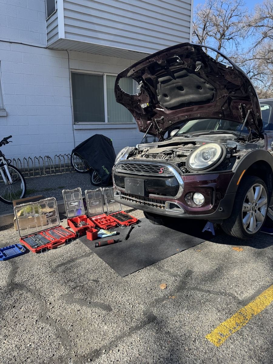 Mini Cooper with the hood up and tool cases spread out in a parking lot