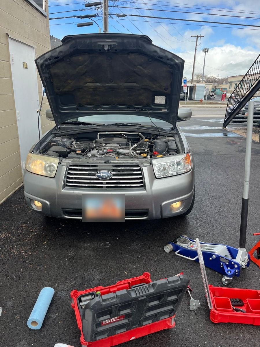 Subaru Forester with the hood up and tools laid out in a driveway